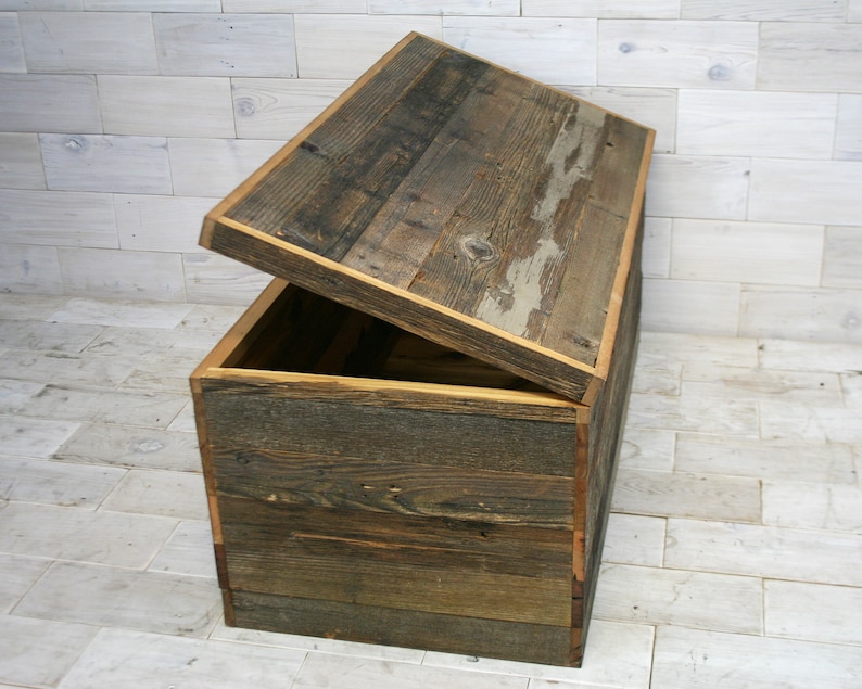 Puede incluir: Un cofre de almacenamiento de madera con tapa con bisagras, hecho de tablones de madera recuperados con un acabado r&uacute;stico. La tapa est&aacute; abierta, revelando el interior del cofre.