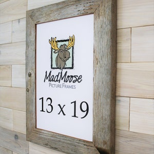 May include: A rustic wood picture frame with a distressed gray finish. The frame is 13 inches by 19 inches and features the Mad Moose Picture Frames logo.