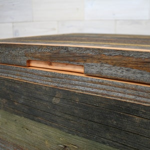 Puede incluir: Primer plano de una caja de madera con una construcci&oacute;n en capas. La capa superior es de madera marr&oacute;n oscura con una tira de madera marr&oacute;n m&aacute;s clara que recorre el borde. La caja est&aacute; hecha de madera recuperada con una variedad de colores y texturas.