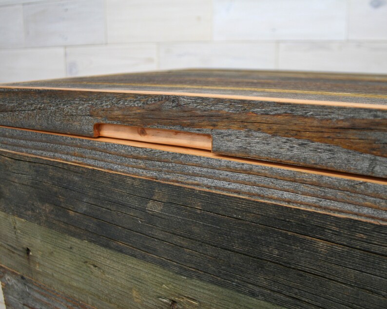 Puede incluir: Primer plano de una caja de madera con una construcci&oacute;n en capas. La capa superior es de madera marr&oacute;n oscura con una tira de madera marr&oacute;n m&aacute;s clara que recorre el borde. La caja est&aacute; hecha de madera recuperada con una variedad de colores y texturas.