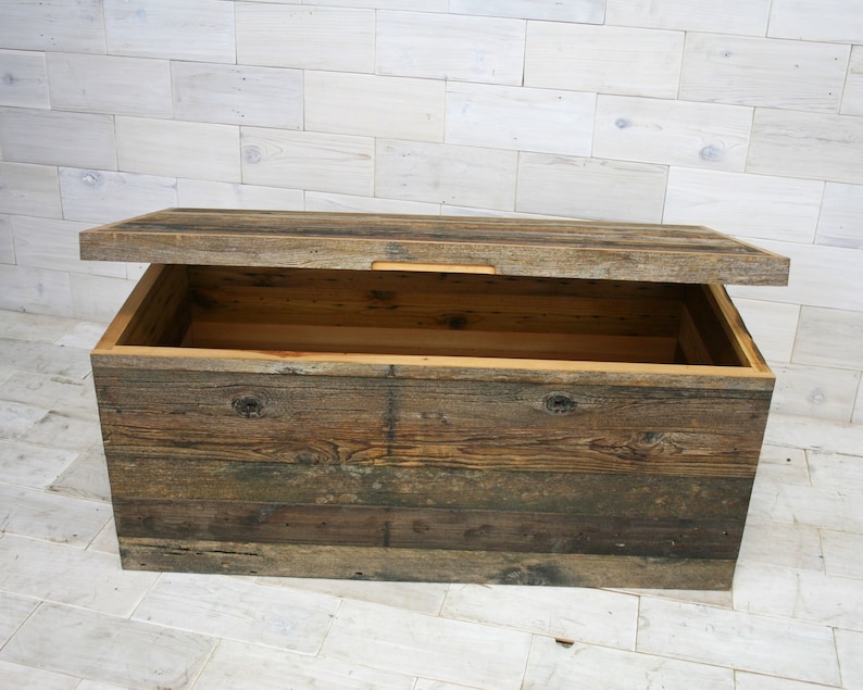 Puede incluir: Un cofre de almacenamiento de madera con tapa con bisagras, hecho de tablones de madera recuperados en tonos marrones, grises y beige. La tapa est&aacute; abierta, revelando el interior vac&iacute;o.