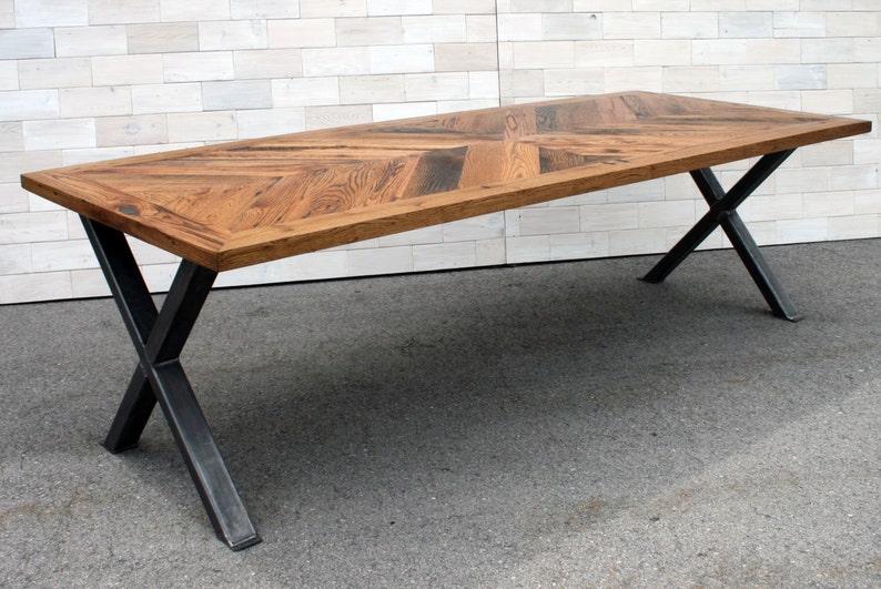 Pu&ograve; includere: Un lungo tavolo in legno con un piano a motivo chevron e gambe a X in metallo nero.
