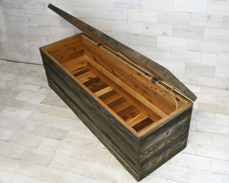 Puede incluir: Un gran cofre de almacenamiento de madera con tapa con bisagras, hecho de madera recuperada con un acabado r&uacute;stico. La tapa est&aacute; abierta, revelando el interior del cofre, que est&aacute; forrado de madera.