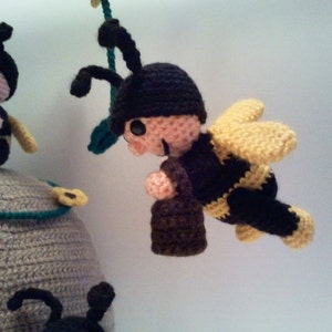 Pu&ograve; includere: Mobile a tema api realizzato all'uncinetto, con un alveare grigio con bordi turchesi e diverse api nere e gialle. Un'ape &egrave; in volo e un'altra &egrave; appollaiata sull'alveare. Le api hanno antenne e cappelli neri.