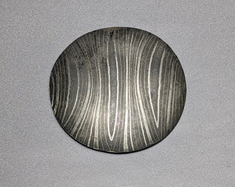May include: A round, silver pendant with a swirling, wood-grain pattern.