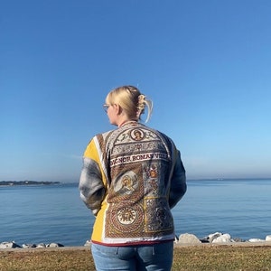 Puede incluir: Una chaqueta con un dise&ntilde;o decorativo y el texto "BIGNOR ROMAN VILLA". La chaqueta tiene un estampado de cuadros amarillos y grises en las mangas y la espalda. La persona lleva vaqueros azules.