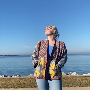 Puede incluir: Chaqueta estampada con bolsillos amarillos en forma de estrella, usada sobre una camiseta azul y vaqueros claros. La chaqueta presenta un dise&ntilde;o geom&eacute;trico en rojo, gris y marr&oacute;n. La persona lleva sandalias negras y gafas, al aire libre en un d&iacute;a soleado.