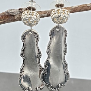 May include: A pair of silver earrings made from vintage silverware with a decorative filigree design. The earrings feature a silver ball with a floral pattern at the top.