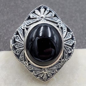 May include: A silver ring with a black onyx gemstone set in a filigree design.