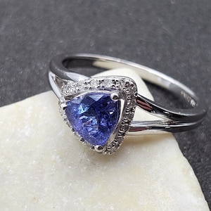 May include: A silver ring with a triangular blue gemstone surrounded by a halo of smaller white gemstones.