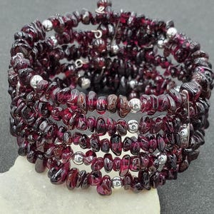May include: A multi-strand bracelet made of small, dark red garnet beads and silver spacer beads. The bracelet is wrapped in a spiral shape and is designed to be adjustable.