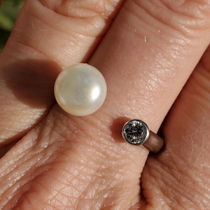 May include: A silver ring with a white pearl and a clear gemstone. The ring is on a person's finger.