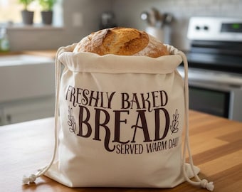 May include: A beige drawstring bread bag with the words "FRESHLY BAKED BREAD SERVED WARM DAILY" printed in brown. The bag contains a loaf of crusty bread. The bag is sitting on a wooden surface.