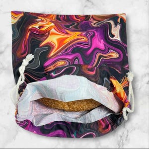 May include: A drawstring bag with a vibrant, swirling pattern in shades of purple, orange, and black. The bag is open, revealing a glimpse of the contents inside. White rope drawstring closure.