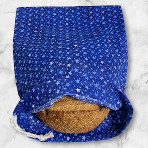 May include: A blue bread bag with a white star pattern holds a loaf of bread. The bag is made of fabric and has a drawstring closure. The bread is a golden brown color and has a crusty texture.