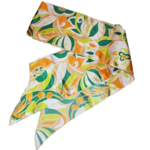 May include: A colorful silk scarf with a vibrant floral pattern in shades of green, orange, and yellow. The scarf is tied in a knot, showcasing its design and texture. The scarf is made of a shiny, silky material.