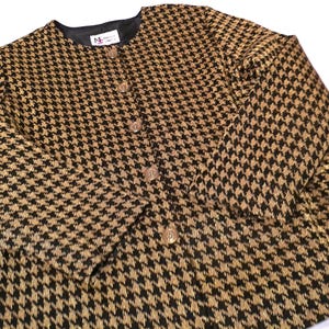 May include: A vintage houndstooth jacket in black and tan. The jacket has a round neckline, long sleeves, and a button-down front. The fabric has a repeating pattern of small, four-pointed shapes.