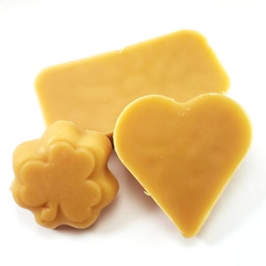 May include: Three pieces of beeswax in different shapes: a rectangle, a heart, and a four-leaf clover. The beeswax is a light golden yellow color.