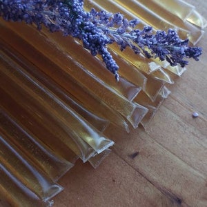 May include: A stack of clear, honey-filled tubes with a sprig of purple lavender flowers on top.