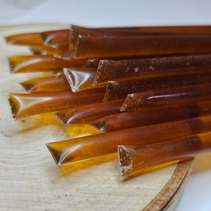 May include: A close-up of a stack of honey sticks. The sticks are clear and amber in color and are arranged in a staggered pattern. The sticks are on a wooden surface.