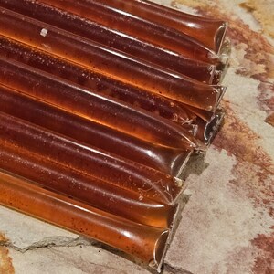 May include: A stack of eight brown honey sticks on a light brown textured surface.