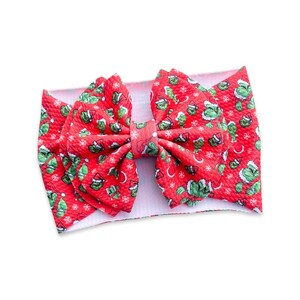 May include: A red headband with a Grinch-themed pattern. The fabric features a repeating design of the Grinch wearing a Santa hat, snowflakes, and Christmas tree leaves. The headband is a large bow style.