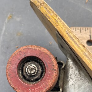 K&ouml;nnte beinhalten: Nahaufnahme eines roten Skateboard-Rads mit einer Metallachse und einer abgenutzten Oberfl&auml;che. Das Rad tr&auml;gt den Schriftzug "ZEPHYR".