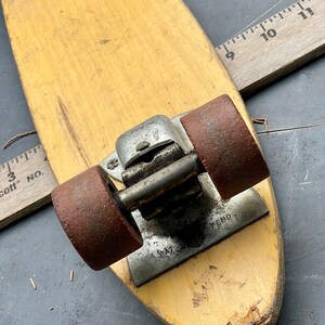 K&ouml;nnte beinhalten: Ein Vintage-Skateboard aus Holz mit zwei roten R&auml;dern und einem Metall-Truck. Das Skateboard hat eine abgenutzte, vergilbte Oberfl&auml;che und einen kleinen Riss an der Unterseite. Der Truck hat eine Metallplatte mit dem Text "PAT. PEND."