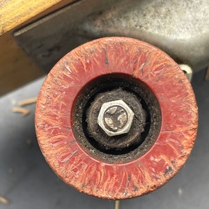 K&ouml;nnte beinhalten: Nahaufnahme eines roten Skateboard-Rads mit abgenutzter Oberfl&auml;che und einer silbernen Metallmutter in der Mitte. Das Rad hat einen schwarzen Gummireifen und ist auf einem Skateboard-Truck montiert.