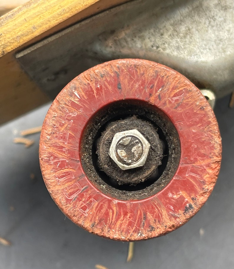 K&ouml;nnte beinhalten: Nahaufnahme eines roten Skateboard-Rads mit abgenutzter Oberfl&auml;che und einer silbernen Metallmutter in der Mitte. Das Rad hat einen schwarzen Gummireifen und ist auf einem Skateboard-Truck montiert.