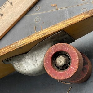 K&ouml;nnte beinhalten: Nahaufnahme eines Vintage-Skateboards aus Holz mit einem roten Gummireifen. Das Rad hat eine Metallachse und eine abgenutzte, verblasste rote Oberfl&auml;che. Das Skateboard ist aus Holz und hat eine Metallhalterung.