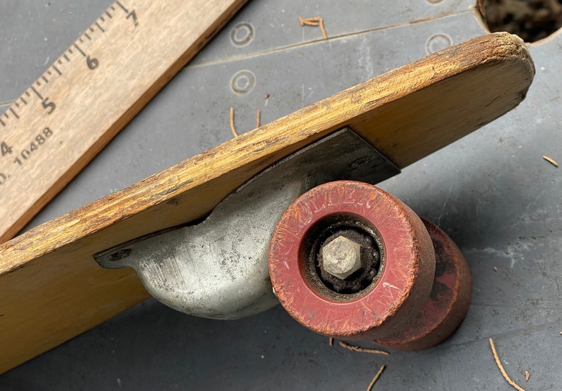 K&ouml;nnte beinhalten: Nahaufnahme eines Vintage-Skateboards aus Holz mit einem roten Gummireifen. Das Rad hat eine Metallachse und eine abgenutzte, verblasste rote Oberfl&auml;che. Das Skateboard ist aus Holz und hat eine Metallhalterung.