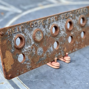 May include: A rusty metal plate with the text "HEAD COPE SAW HEAD CO" and several circular holes. The plate is weathered and has a brown and gray patina.