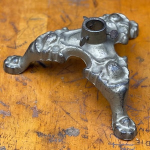 May include: A silver metal Christmas tree stand with three ornate legs. The stand has a round top with a screw for attaching a tree.