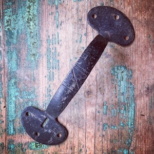 May include: A black metal door handle with a decorative design. The handle is attached to a wooden surface with a light blue and brown paint finish.