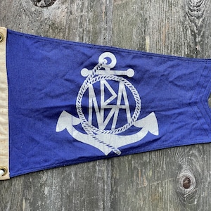 May include: A blue pennant flag with a white anchor and rope design. The anchor has the letters "NBA" inside the rope circle.