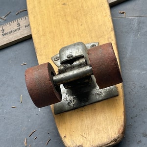 K&ouml;nnte beinhalten: Ein Vintage-Skateboard aus Holz mit zwei rostigen R&auml;dern und einem Metall-Truck. Das Skateboard ist abgenutzt und hat ein paar Kratzer.