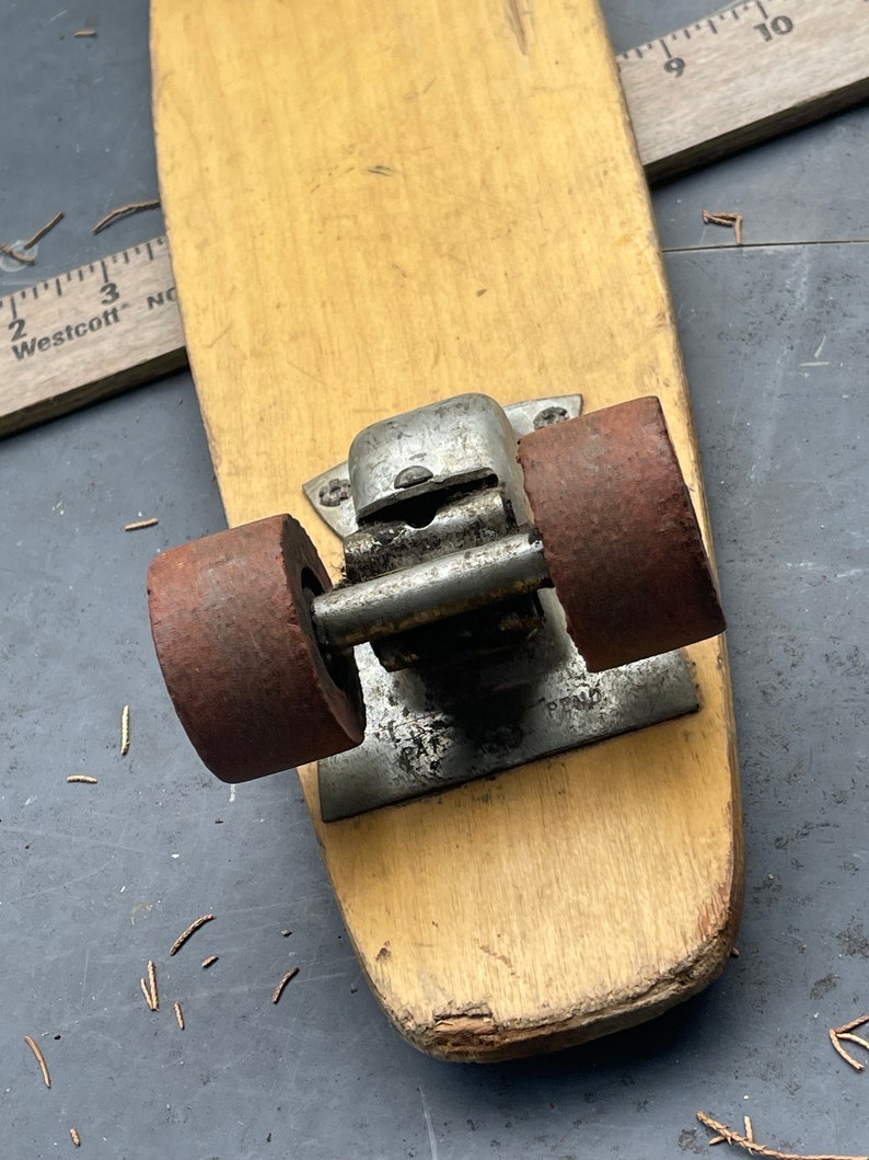 K&ouml;nnte beinhalten: Ein Vintage-Skateboard aus Holz mit zwei rostigen R&auml;dern und einem Metall-Truck. Das Skateboard ist abgenutzt und hat ein paar Kratzer.