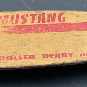 K&ouml;nnte beinhalten: Vintage Holz-Roller-Derby-Brett mit roter und wei&szlig;er Farbe und den aufgedruckten Worten "Mustang Roller Derby No. 15".