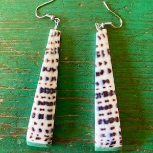 May include: A pair of long, dangle earrings made from a white and brown shell with a green edge. The earrings have silver hooks.