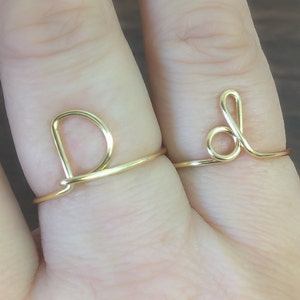 May include: Two gold wire rings with the letters D and L formed in the wire. The rings are worn on the index and middle fingers of a hand.