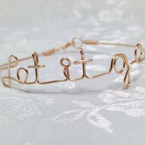 May include: Gold wire bracelet with the words "Let it go" written on it.