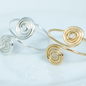 May include: Two wire bracelets with spiral designs. One bracelet is silver and the other is gold.