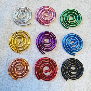 May include: Nine colorful metal spiral ornaments in silver, pink, green, gold, purple, blue, copper, red, and black. Each spiral is a unique, eye-catching design, perfect for crafts or decorative purposes.