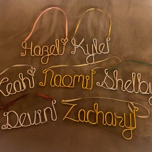 May include: Handmade wire name ornaments in gold and silver tones, each with a ribbon for hanging. Names include Hazel, Kyle, Leah, Naomi, Shelby, Devin, and Zachary. A personalized gift idea for Christmas or other special occasions.