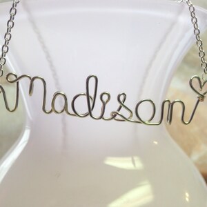 May include: Silver necklace with the name "Madison" spelled out in wire with a small heart charm at the end.