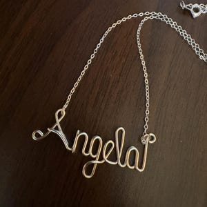 May include: A silver chain necklace with a wire-wrapped name pendant that says "Angela".