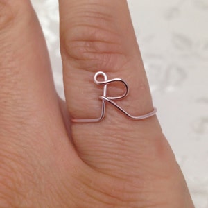 May include: A rose gold wire ring with the letter "R" formed in the center.