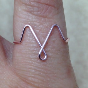 May include: A rose gold wire ring shaped like a heart beat.