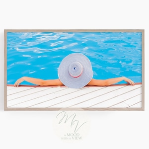 Puede incluir: Una mujer con un sombrero de sol a rayas azules y blancas se relaja junto a una piscina. El agua de la piscina es de un azul brillante y la plataforma es de madera blanca.